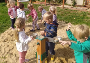 dzieci bawia się w piaskownicy przy wadze na terenie ogródka "Słoneczna Akademia"